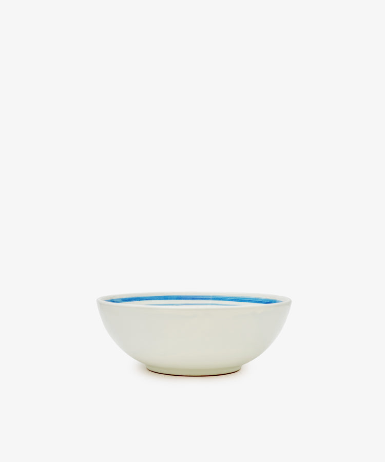 The Folk Cereal Bowl, Jester features a white ceramic body with a hand-painted blue interior rim by an Italian ceramist, adding whimsical charm to your table. Shown on a plain white background.