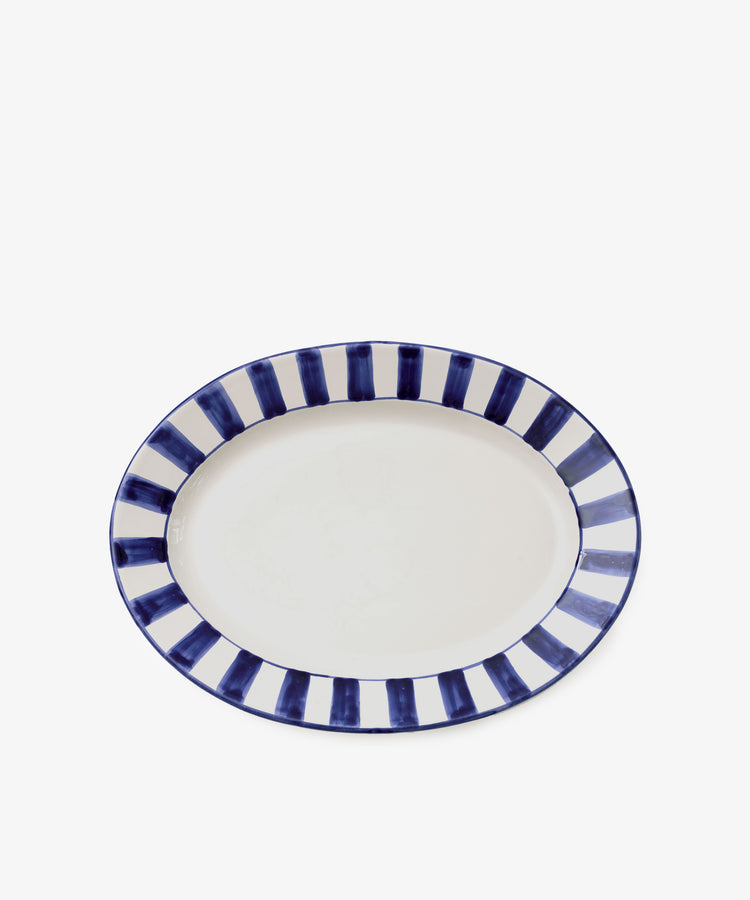 The Julius Oval Serving Platter features a white ceramic center and bold, hand-painted blue striped border, shown from above against a plain white background.
