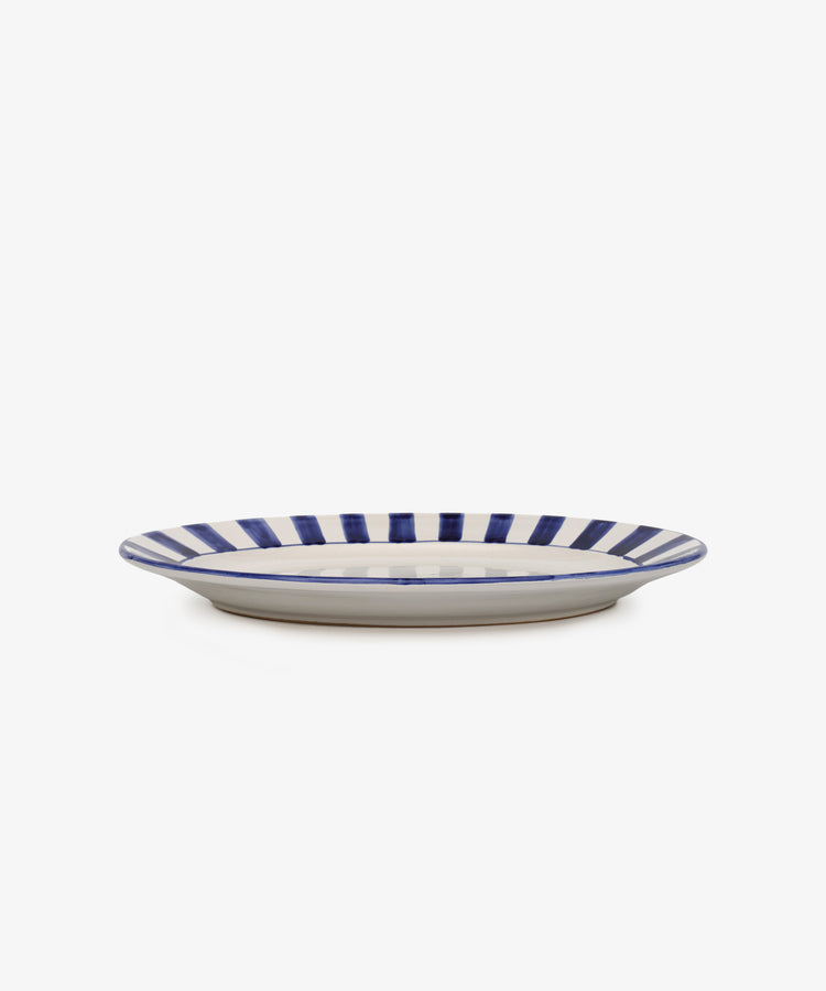 The Julius Oval Serving Platter features a white ceramic base with bold, hand-painted blue vertical stripes along the rim, displayed against a plain white background.
