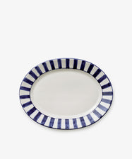 The Julius Oval Serving Platter features a white center with bold, hand-painted blue stripes around the border on a sleek white ceramic background.