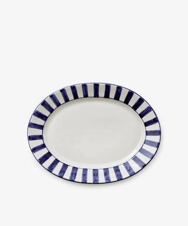 The Julius Oval Serving Platter features a white center with bold, hand-painted blue stripes around the border on a sleek white ceramic background.