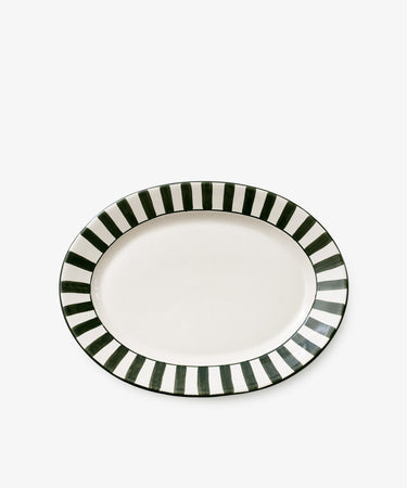 The Julius Oval Serving Platter is a white ceramic dish with an oval shape, featuring a bold border of hand-painted black and white vertical stripes.