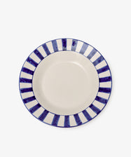 The Julius Serving Platter is a round ceramic piece with a cream center and a border of alternating dark blue and white stripes, ideal for serving appetizers or desserts.