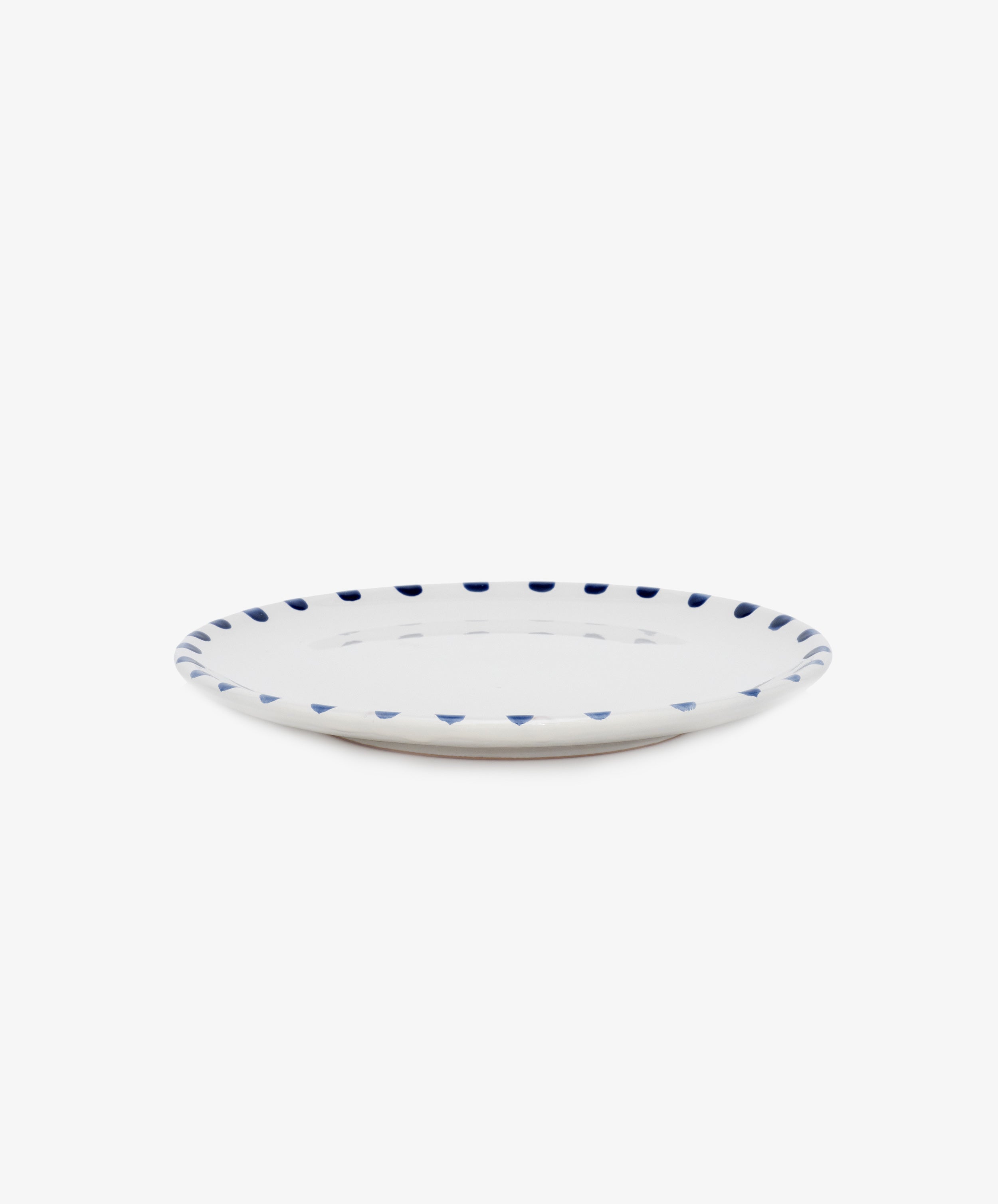 Nina Small Plate. White glazed ceramic plate with blue painted rim details, angled side view.