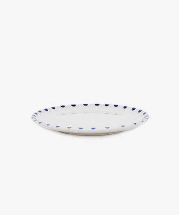 Nina Small Plate. White glazed ceramic plate with blue painted rim details, angled side view.