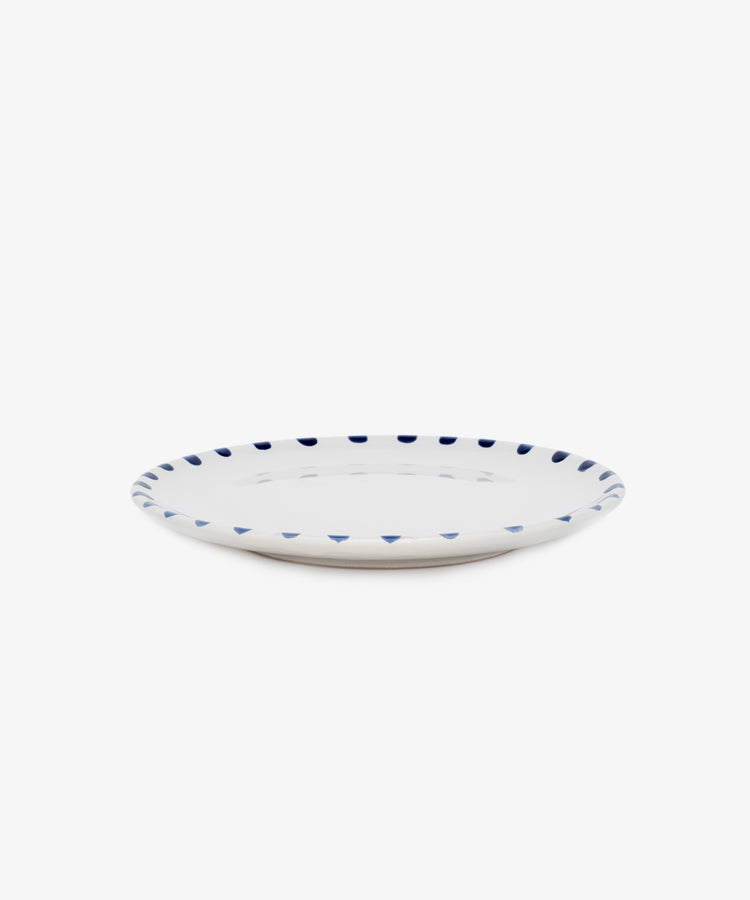 Nina Small Plate. White glazed ceramic plate with blue painted rim details, angled side view.