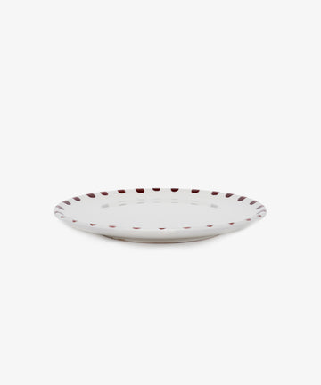 Nina Small Plate. White glazed ceramic plate with burgundy painted rim details, angled side view.