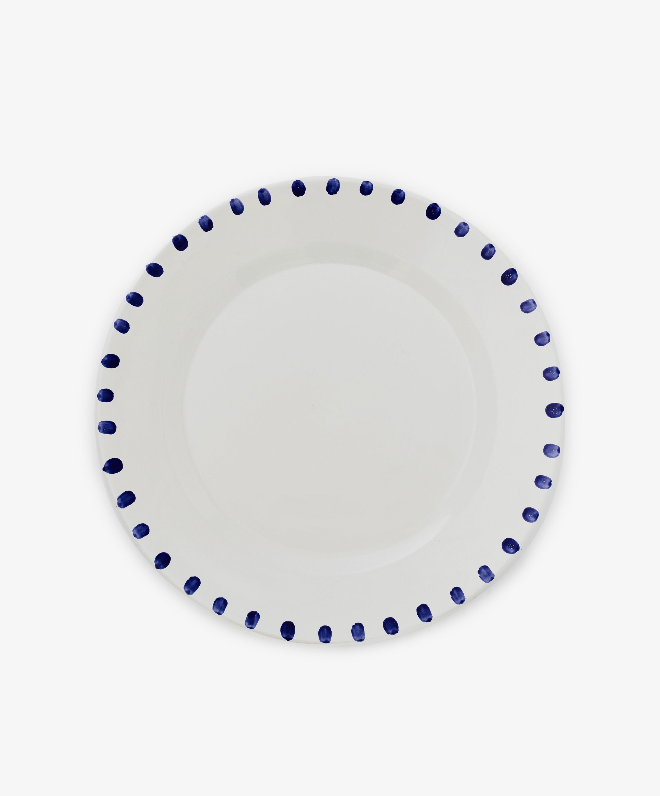 The Nina Serving Plate is a white ceramic plate featuring evenly spaced blue dots around the rim, shown against a plain white background.