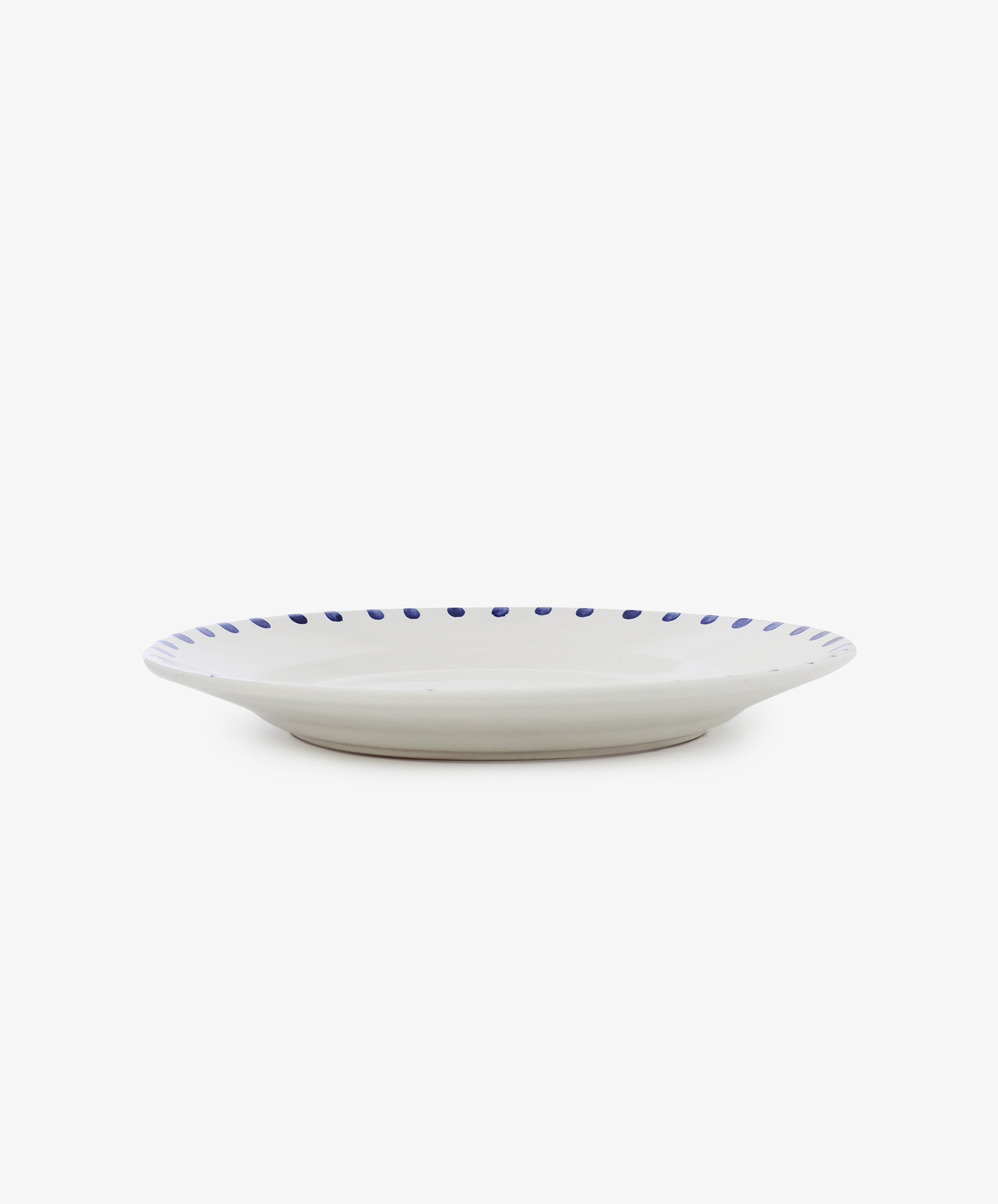 The Nina Serving Plate is a white ceramic plate featuring a blue dotted rim, shown from the side against a plain white background.