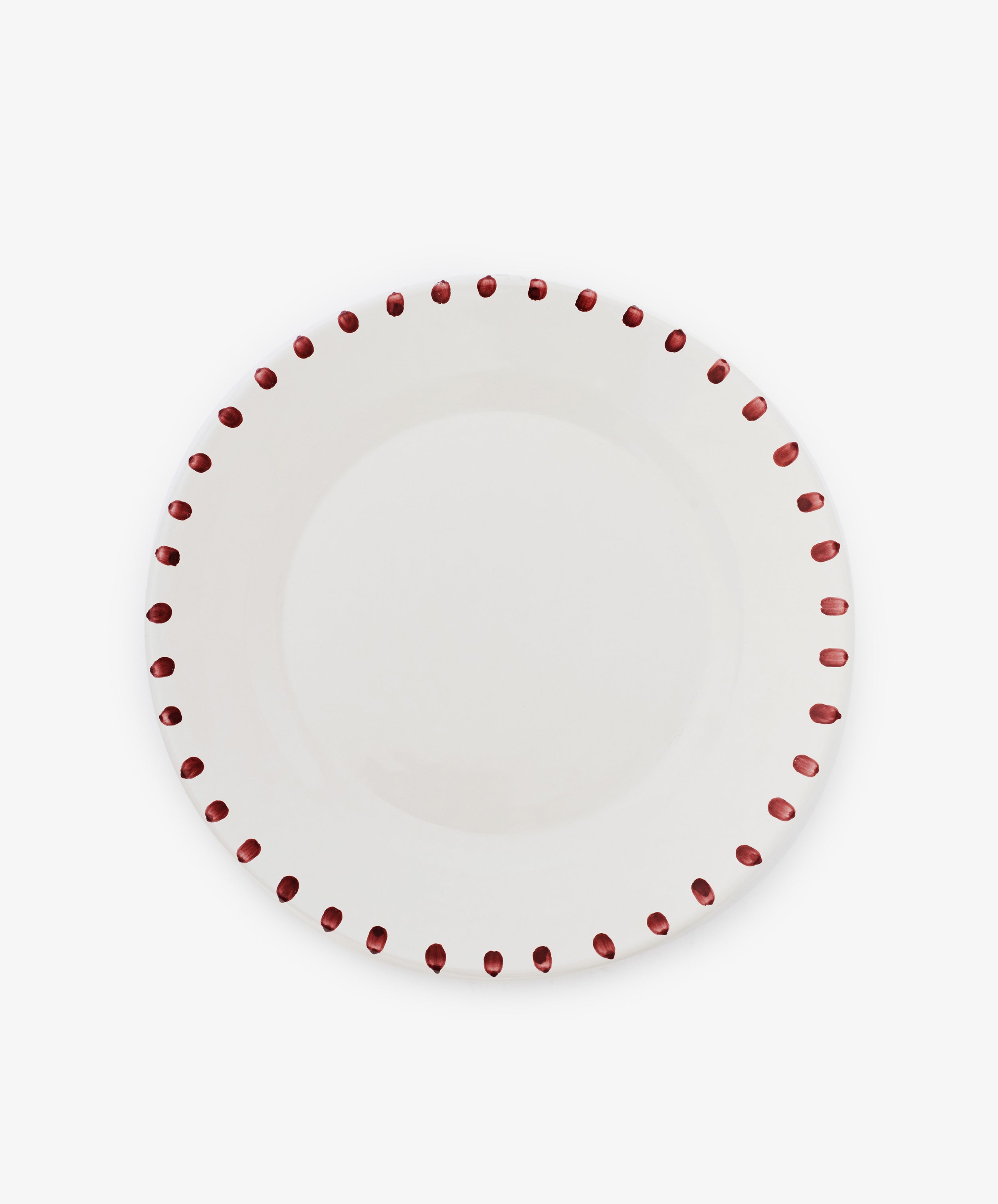 The Nina Serving Plate is a white ceramic plate with evenly spaced red dots around the rim, shown on a plain white background. Its simple, elegant design coordinates perfectly with Nina bowls.