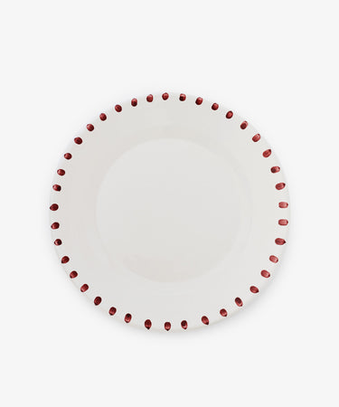 The Nina Serving Plate is a white ceramic plate with evenly spaced red dots around the rim, shown on a plain white background. Its simple, elegant design coordinates perfectly with Nina bowls.