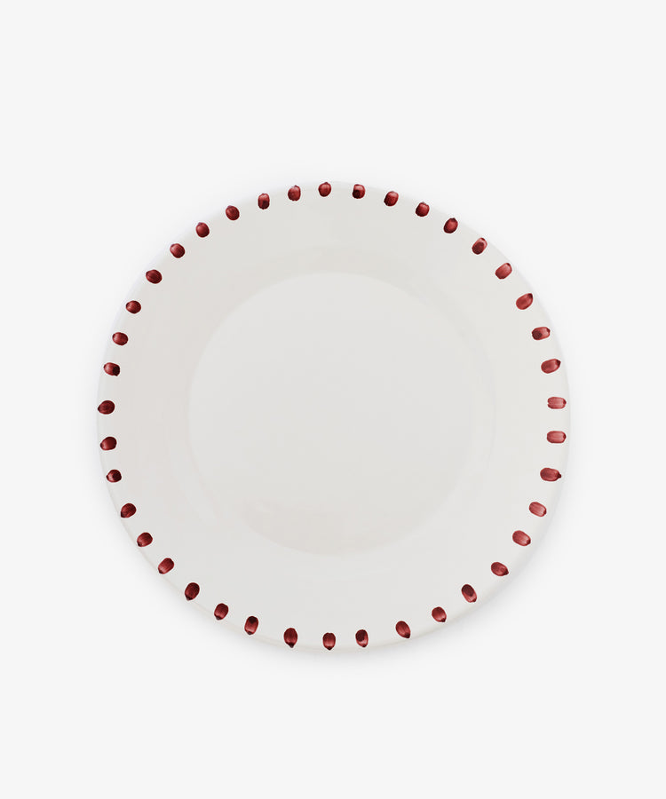 The Nina Serving Plate is a white ceramic plate with evenly spaced red dots around the rim, shown on a plain white background. Its simple, elegant design coordinates perfectly with Nina bowls.