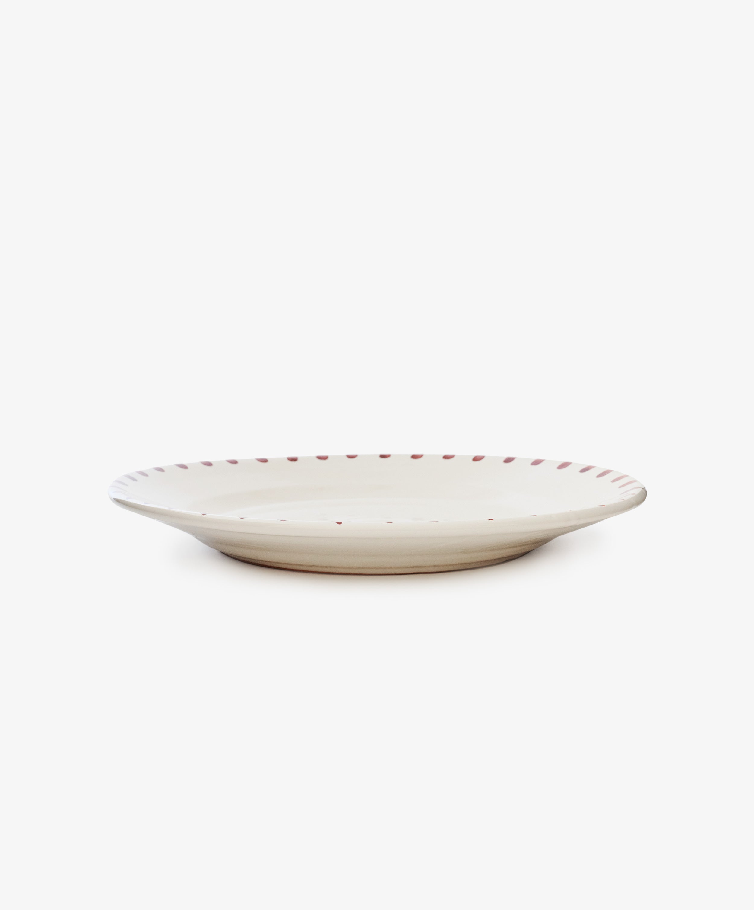 The Nina Serving Plate is a round, shallow white ceramic plate with a slightly raised rim and small red dots along the edge, shown on a plain white background.