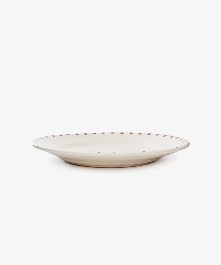 The Nina Serving Plate is a round, shallow white ceramic plate with a slightly raised rim and small red dots along the edge, shown on a plain white background.
