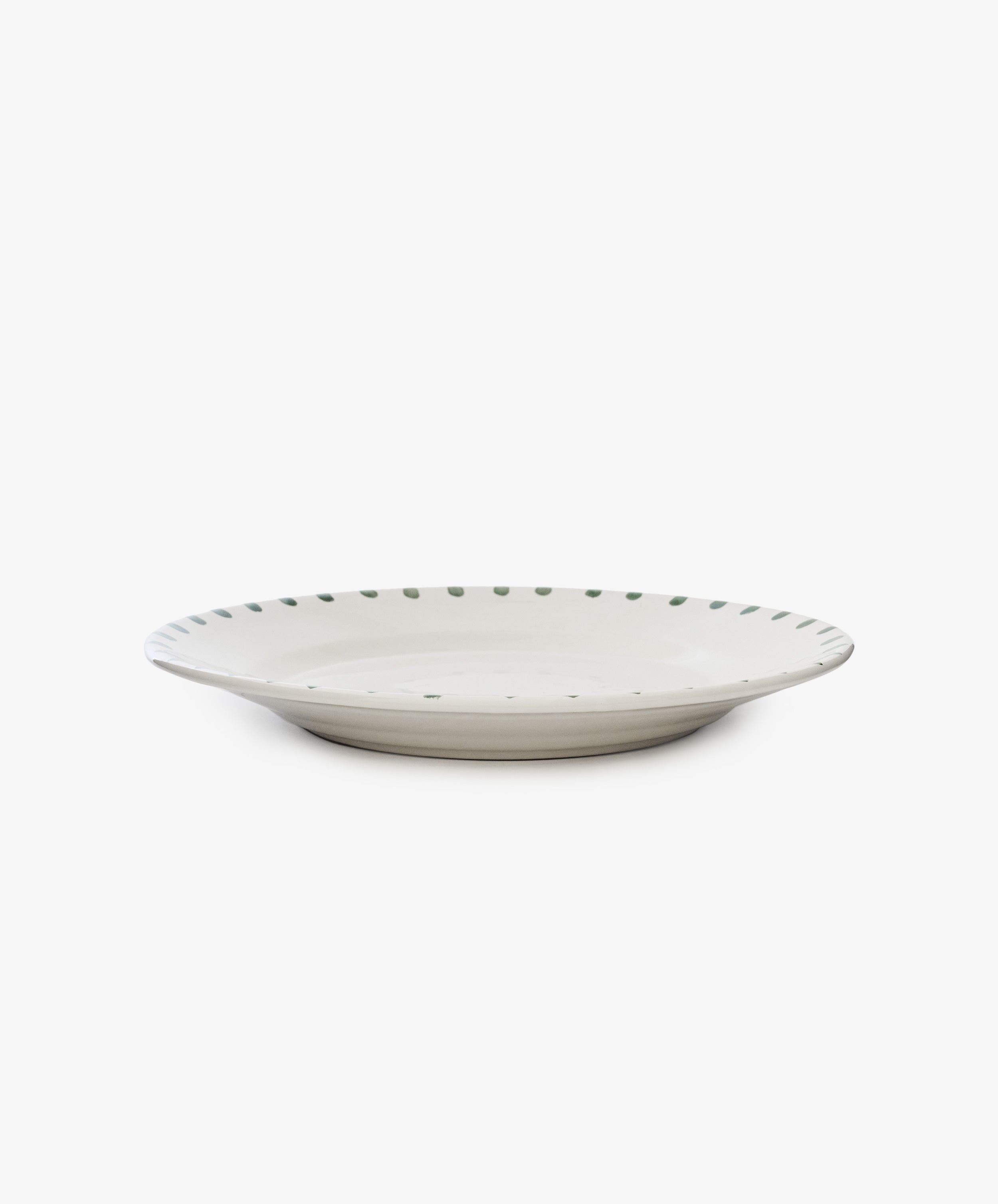 The Nina Serving Plate features a shallow, round design with a white base and a rim accented by evenly spaced green dots, shown against a plain white background.
