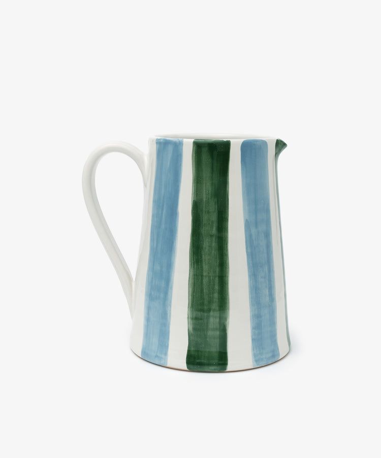 The Mina Jug is an artisanal ceramic pitcher with a handle, featuring hand-painted blue and green vertical stripes on a white background—a charming addition to any table setting.