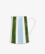 The Mina Jug is a white ceramic pitcher with a curved handle, hand-painted with elegant vertical green, blue, and white stripes—an Italian design shown against a plain white background.