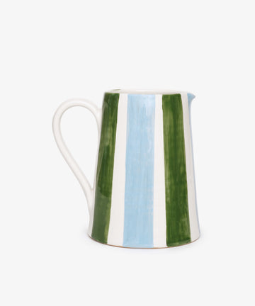 The Mina Jug is a hand-painted Italian piece featuring vertical green, blue, and white stripes, with a handle and spout, displayed against a plain white background.
