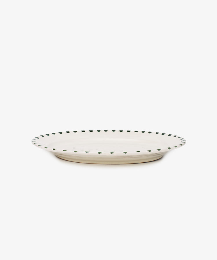 The Nina Oval Serving Platter is a hand-glazed, off-white ceramic plate with a slightly raised rim and small dark green dots—an entertaining essential perfect for serving.