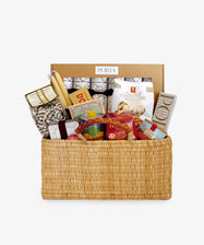 The All-Out Holiday Hamper is a woven basket packed with gourmet pasta, breadsticks, cookies, and snacks—making it the perfect luxury Christmas gift. A cardboard box labeled 