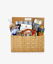 The Holiday Pantry gift basket features risotto rice, pasta, canned goods, snacks, and olive oil in a woven basket displayed before a box labeled PORTA.