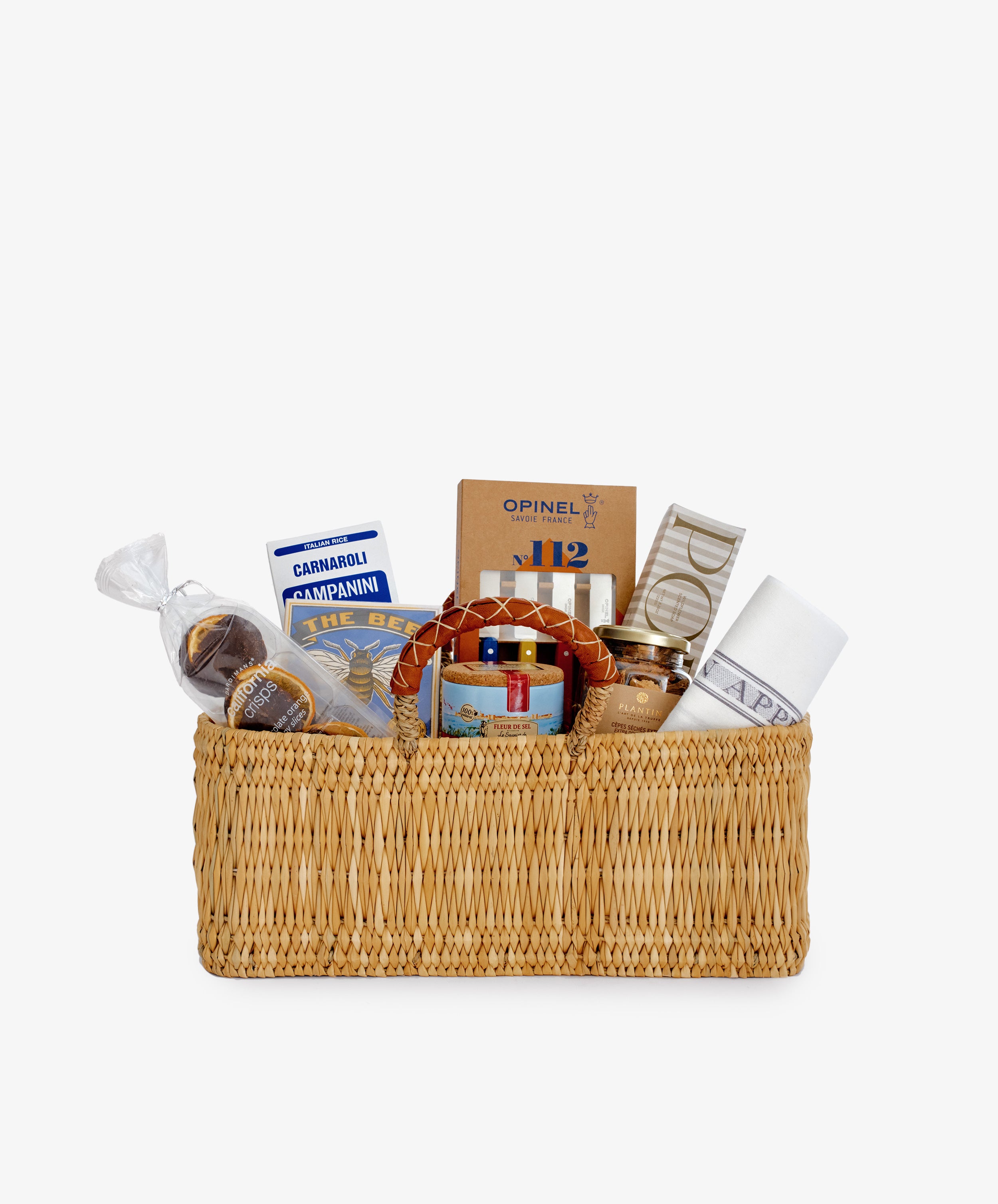 The Cooks Companion is a gourmet gift hamper featuring a woven basket filled with gourmet food items, risotto rice, kitchen utensils, and a white napkin, all elegantly arranged against a plain background.