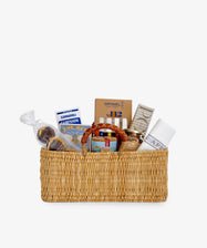 The Cooks Companion is a gourmet gift hamper featuring a woven basket filled with gourmet food items, risotto rice, kitchen utensils, and a white napkin, all elegantly arranged against a plain background.