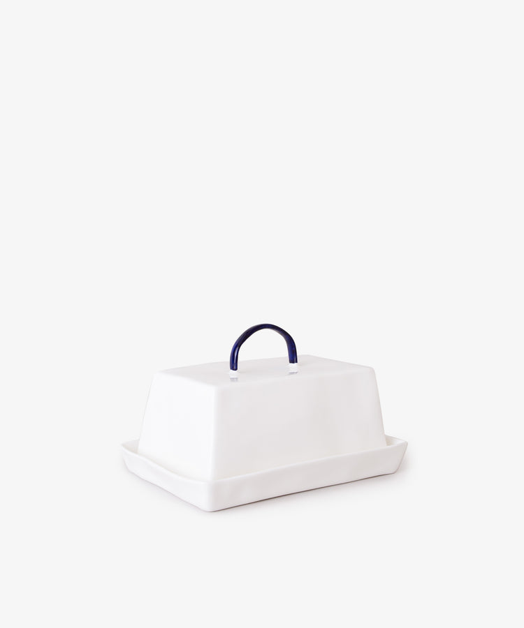 The Butterdish is a rectangular white Feldspar ceramic piece featuring a dark blue handle on the lid, set on a matching tray against a plain background, highlighting its elegant simplicity.