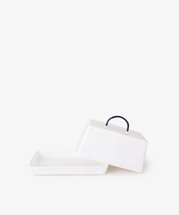 The Butterdish is a rectangular white ceramic piece with elegant simplicity, featuring a Feldspar-inspired matching lid and dark blue handle. Shown with the lid beside the base on a plain white background.