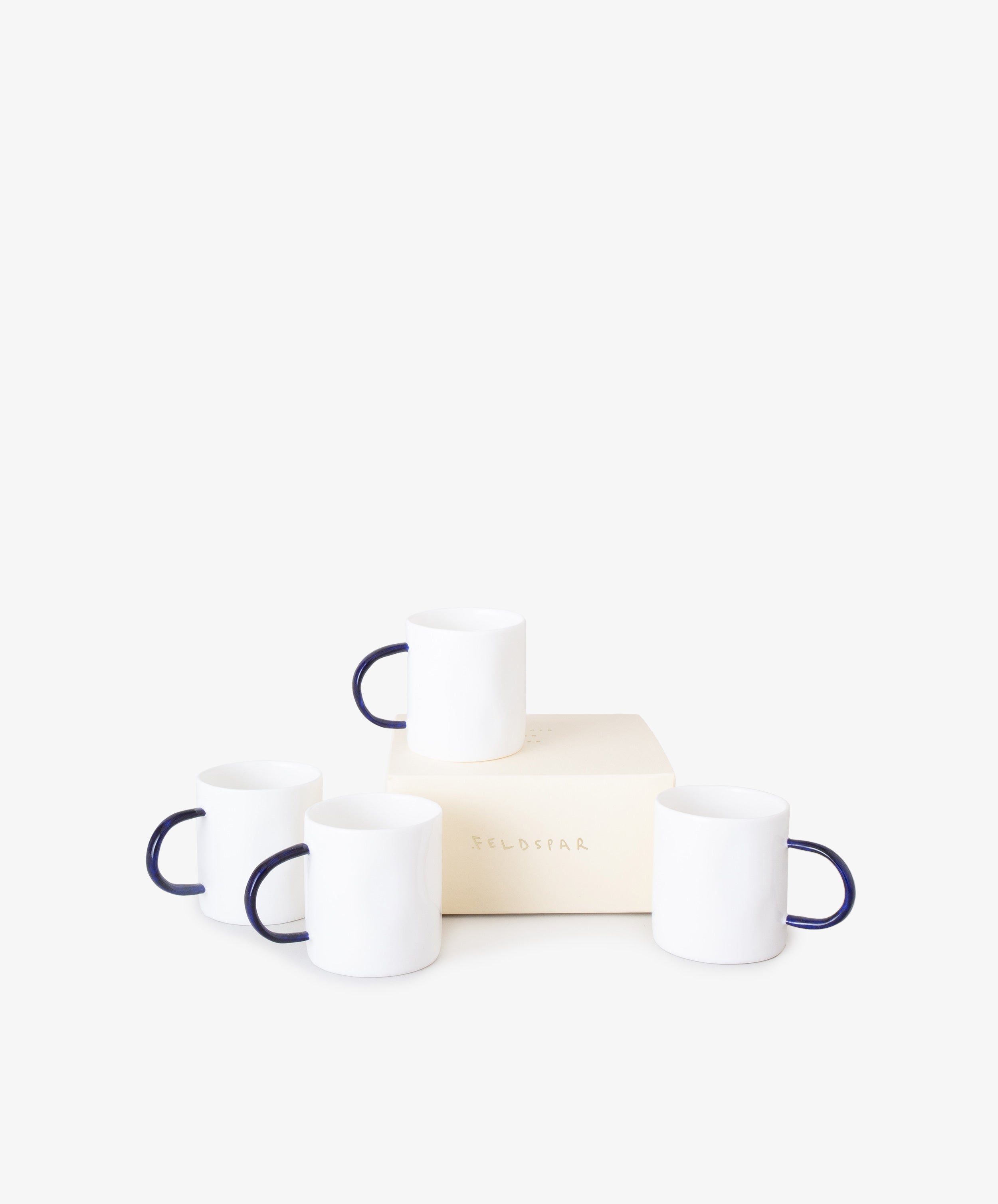 Grouping of four white china espresso cups with thin, rounded cobalt blue handles and Feldspar cream box.