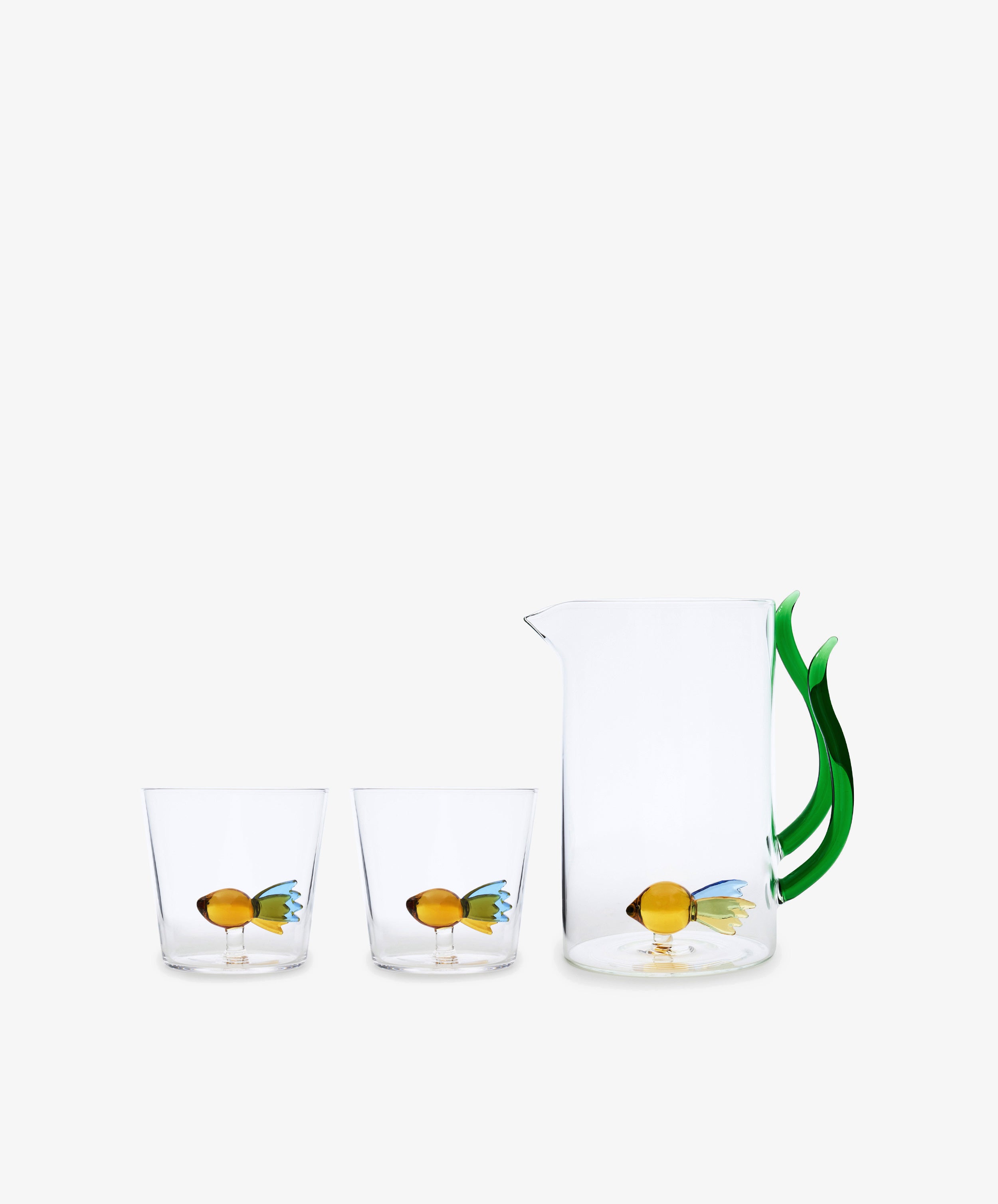 A clear handcrafted glass pitcher with a green handle and two Ichendorf Milano Fish Tumblers, each featuring a decorative fish design at the base.