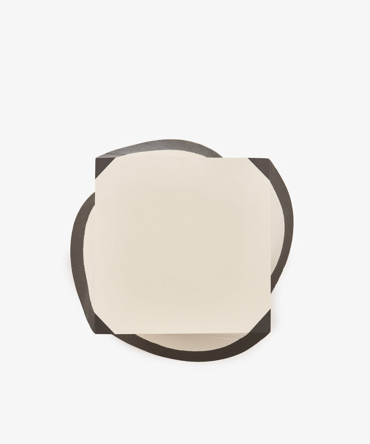 A sheet from the Spiral Notepad, distinguished by its cut corners and square shape, rests on an irregular black surface against a white background.