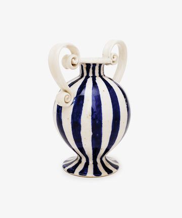The Cyrene Bud Vase is a hand-thrown blue-and-white vase with bold vertical stripes and two large sculptural scroll handles on each side.
