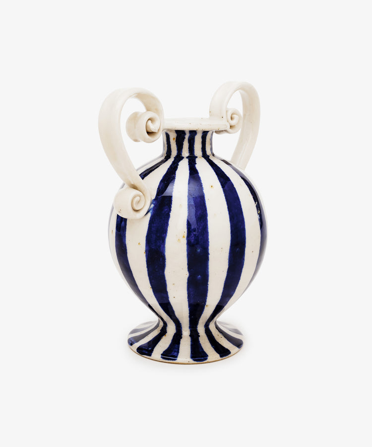 The Cyrene Bud Vase is a hand-thrown blue-and-white vase with bold vertical stripes and two large sculptural scroll handles on each side.