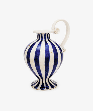 The Delphinia Bud Vase features blue-and-white vertical stripes, a wide body, narrow neck, flared rim, and an elegant curved sculptural scroll handle.