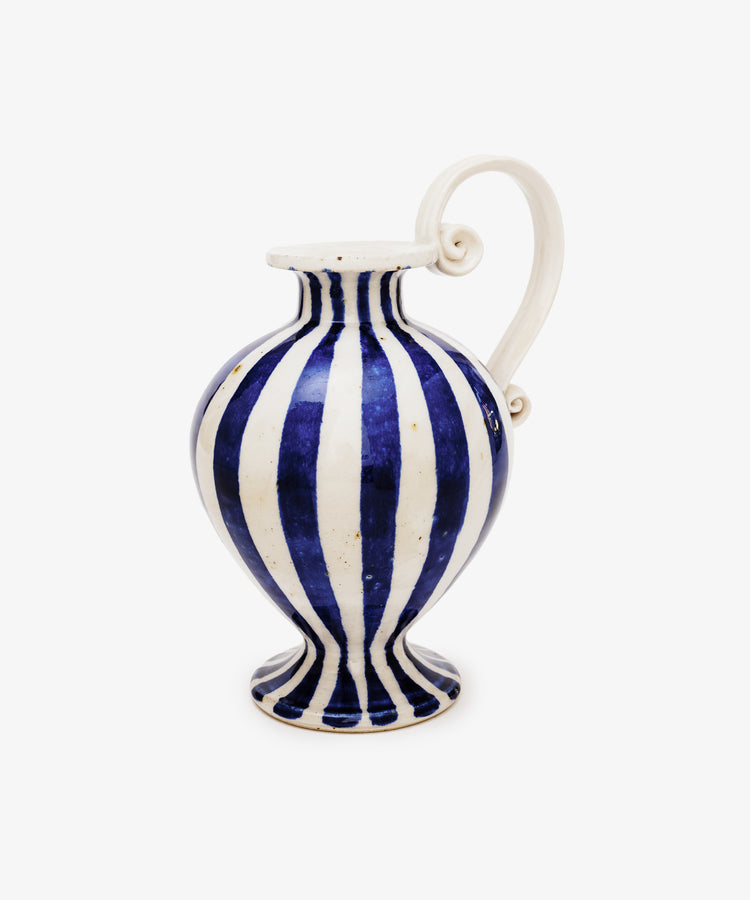 The Delphinia Bud Vase features blue-and-white vertical stripes, a wide body, narrow neck, flared rim, and an elegant curved sculptural scroll handle.