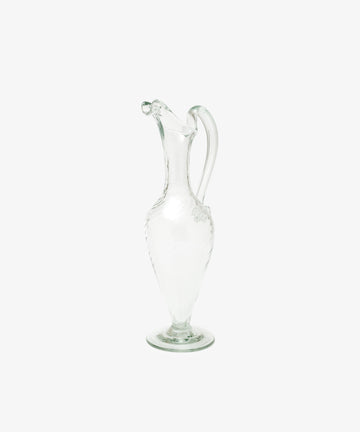 The Alba Vase, a hand-blown glass piece with a narrow neck, curved handle, and decorative spout, stands upright on a plain white background, highlighting its elegant and unique craftsmanship.
