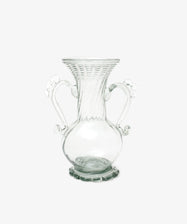 The Camilla Vase is a clear, hand-blown glass piece with a flared rim, two ornate handles, a round base, and decorative detailing—offering a unique artisan touch to your decor.