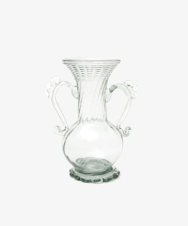 The Camilla Vase is a clear, hand-blown glass piece with a flared rim, two ornate handles, a round base, and decorative detailing—offering a unique artisan touch to your decor.