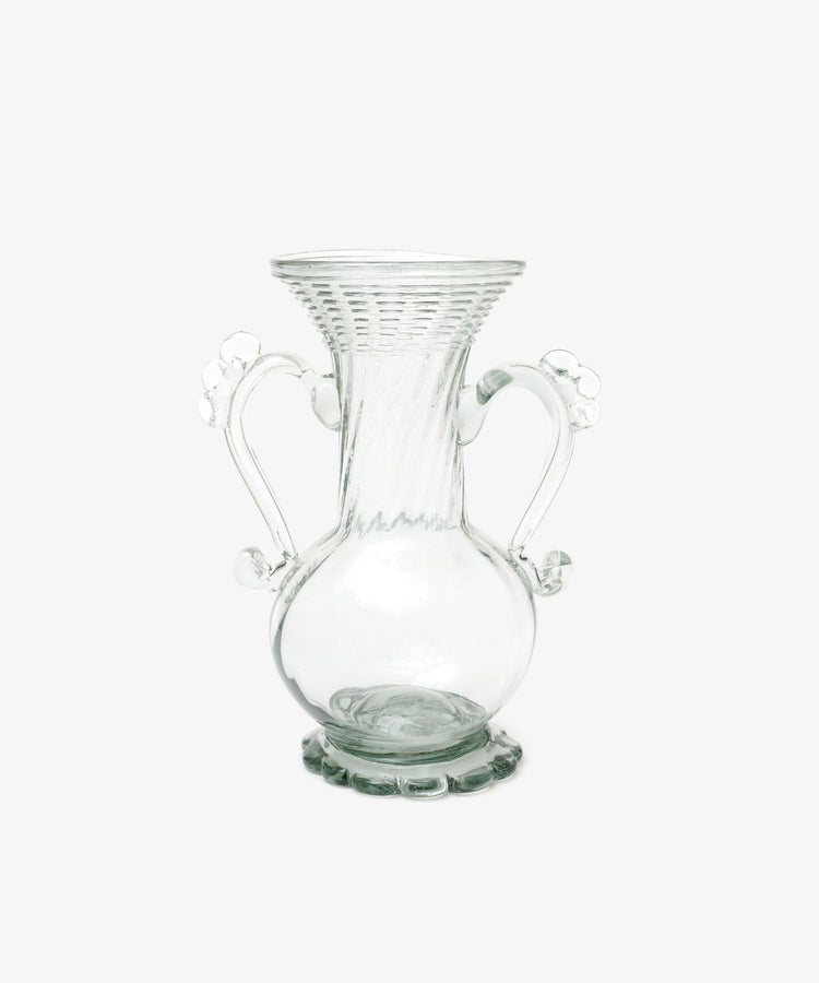 The Camilla Vase is a clear, hand-blown glass piece with a flared rim, two ornate handles, a round base, and decorative detailing—offering a unique artisan touch to your decor.