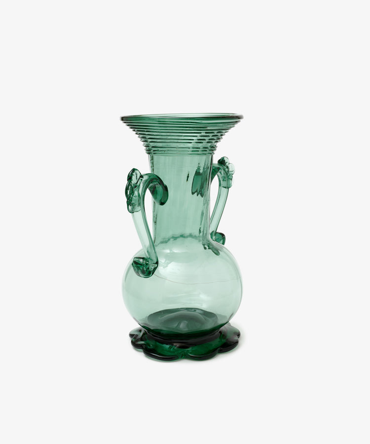Individually crafted, the Camilla Vase is a green glass piece with two ornate handles and a wide, flared rim, showcasing unique artistry against a plain white background.