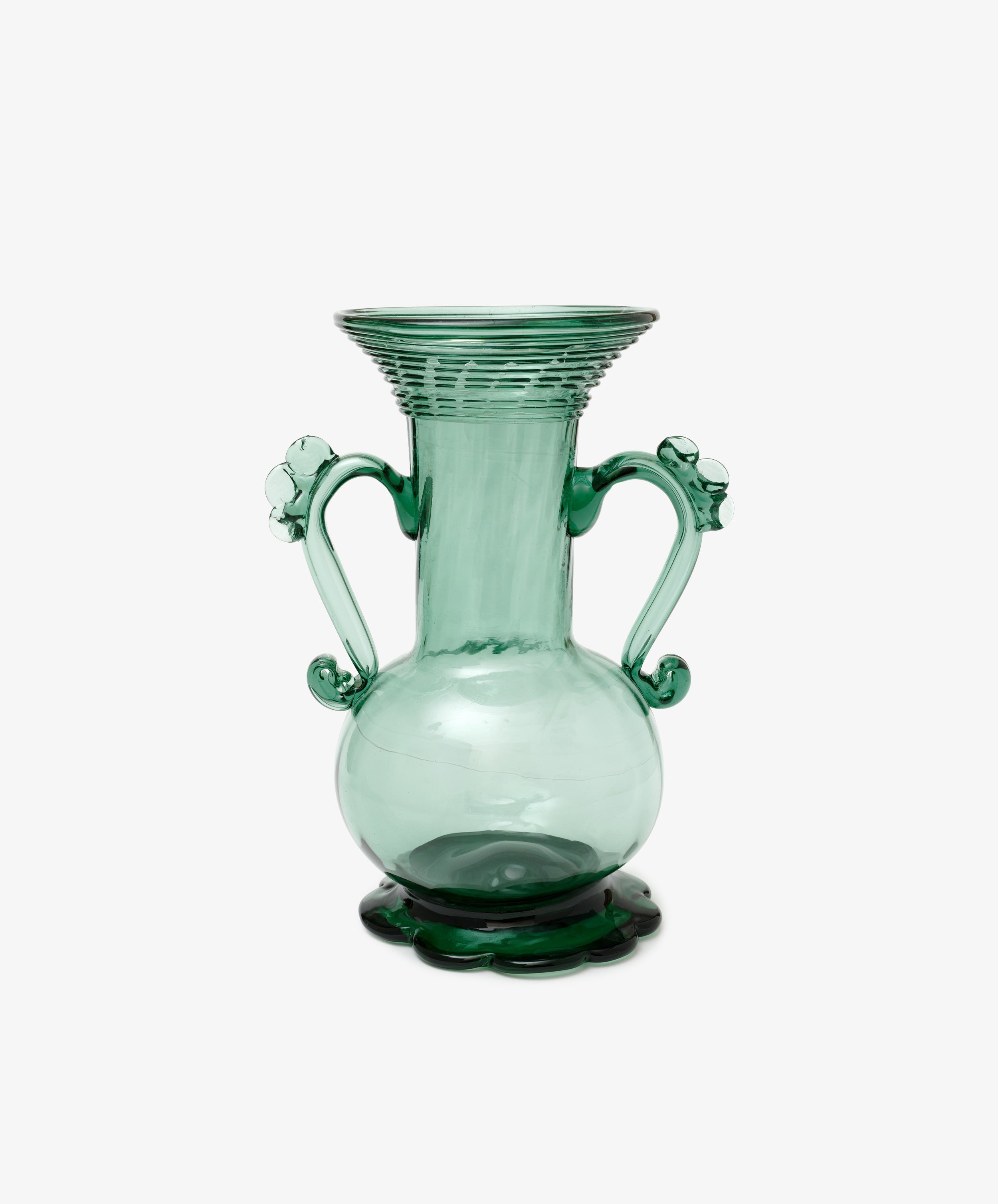 The Camilla Vase is a green hand-blown glass piece with two decorative handles, a wide flared rim, and stands on a scalloped base—individually crafted and set against a white background.