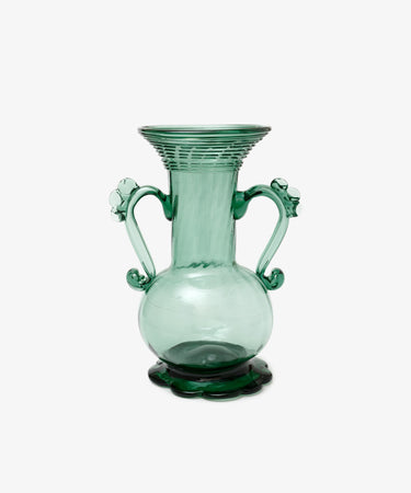 The Camilla Vase is a green hand-blown glass piece with two decorative handles, a wide flared rim, and stands on a scalloped base—individually crafted and set against a white background.