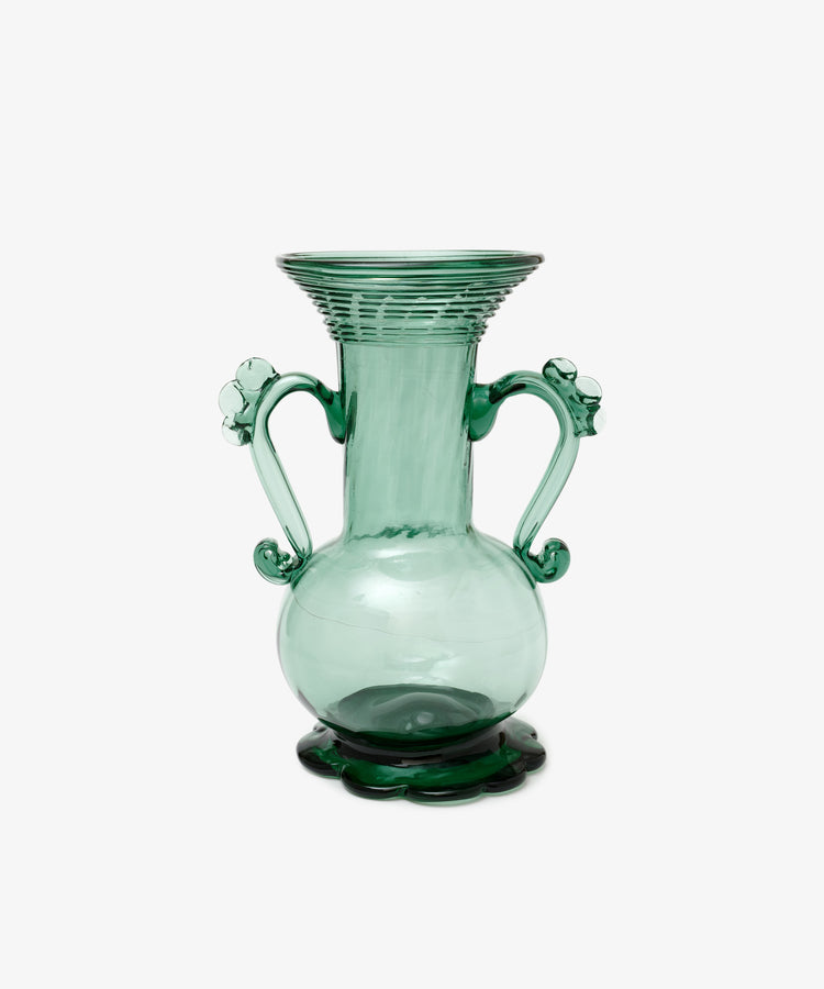 The Camilla Vase is a green hand-blown glass piece with two decorative handles, a wide flared rim, and stands on a scalloped base—individually crafted and set against a white background.
