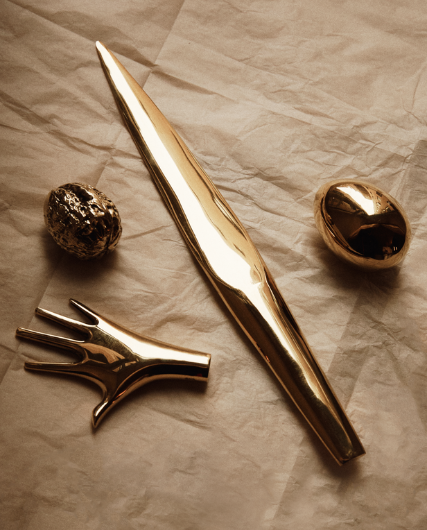 The Walnut Paperweight—a gold-toned metallic object—rests elegantly on crumpled, light paper, echoing the playful sophistication and artistic craftsmanship of a desk sculpture from the Auböck workshop.