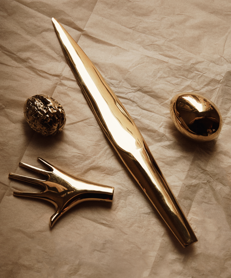 The Walnut Paperweight—a gold-toned metallic object—rests elegantly on crumpled, light paper, echoing the playful sophistication and artistic craftsmanship of a desk sculpture from the Auböck workshop.