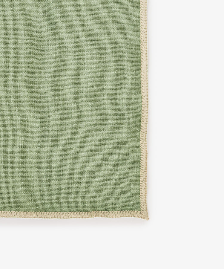 A close-up of the Corte Napkin, Set of 6, in green eco-friendly linen with beige stitched edges, set against a white background—ideal for adding elegance to your table as placemats or napkins.