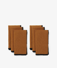 Luri Napkin. Two rows of three napkins in golden brown linen, with black stitched edges.