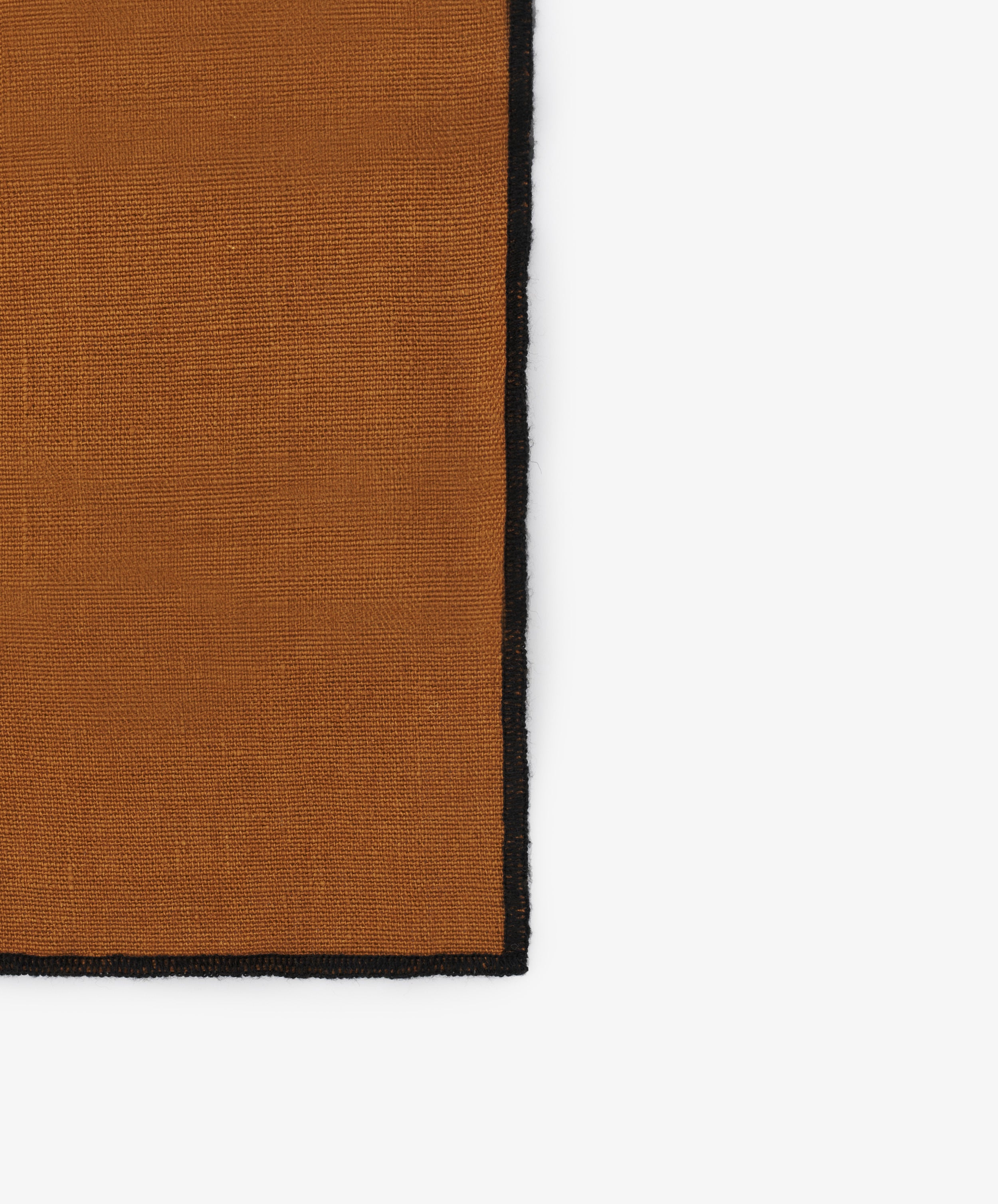 Close-up of black stitched edges on the golden brown linen Luri Napkin.