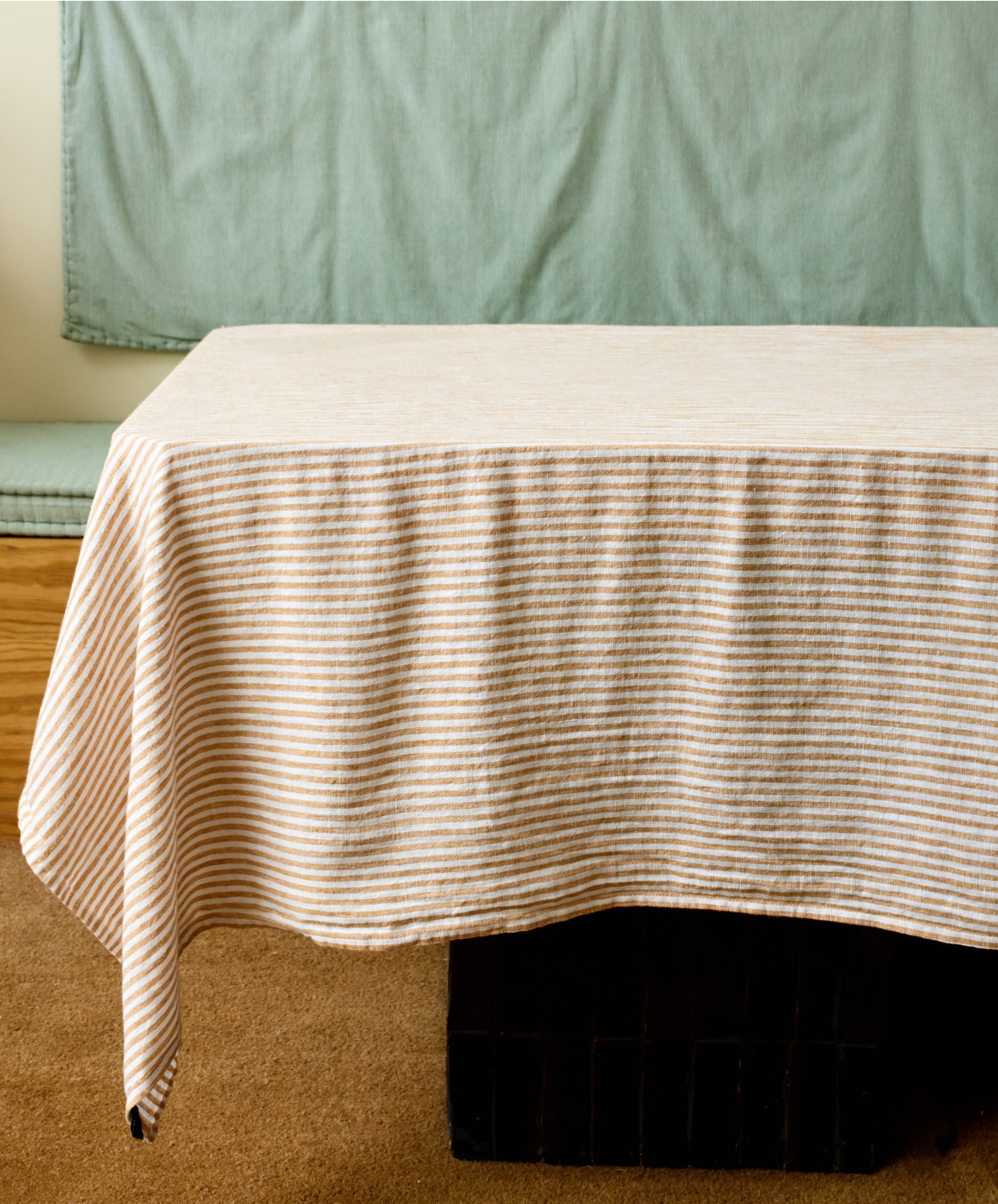 Vezzani Tablecloth in orange and white striped linen, draped on table in studio.